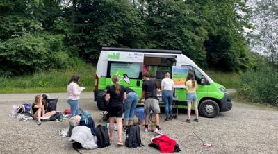 Ein Gruppe Schüler steht und sitzt vor dem offenen Umweltmobil.